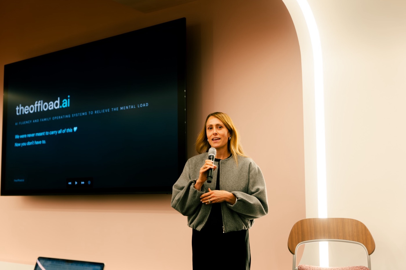 Holly speaking with a microphone in front of a theoffload.ai slide that reads: we were never meant to carry all of this.