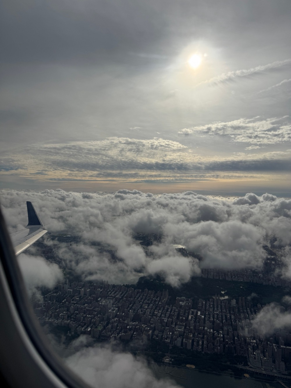 Manhattan seen through an airplane window, the wing tip over the clouds and Central Park below.