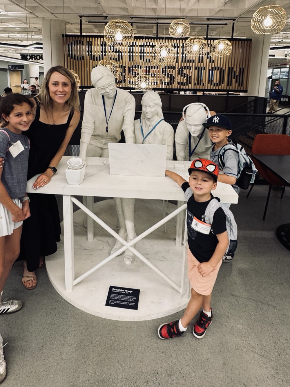 Holly and her three kids beside a marble sculpture of a team at a laptop, on a visit to the Amazon office.