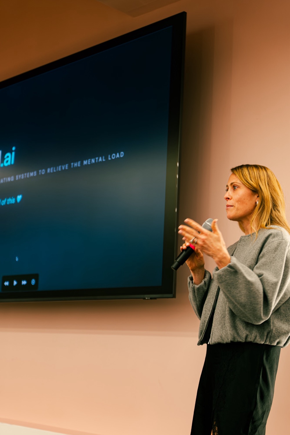 Holly presenting with a microphone beside a screen showing the theoffload.ai title slide.